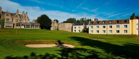 Un parcours de golf doté d’un club-house traditionnel, d’un bâtiment en pierre et d’un bâtiment moderne avec de nombreuses fenêtres.