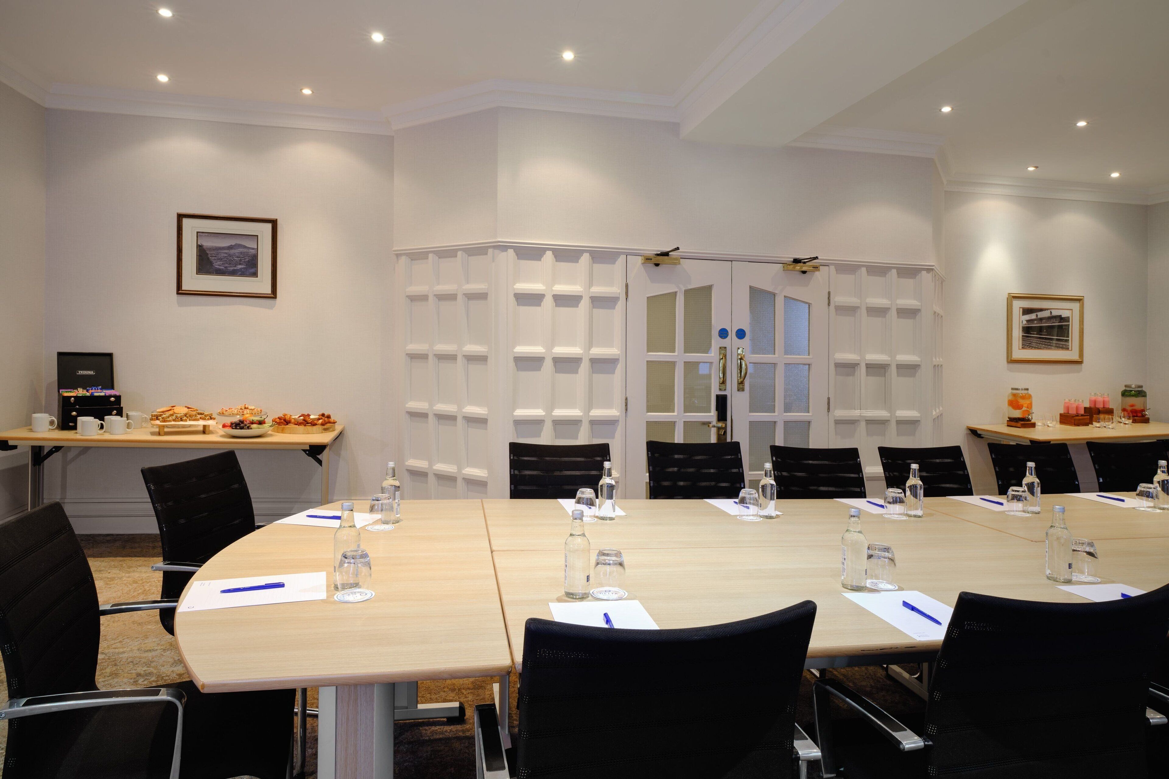 A conference room with a long table, black chairs, and water bottles.