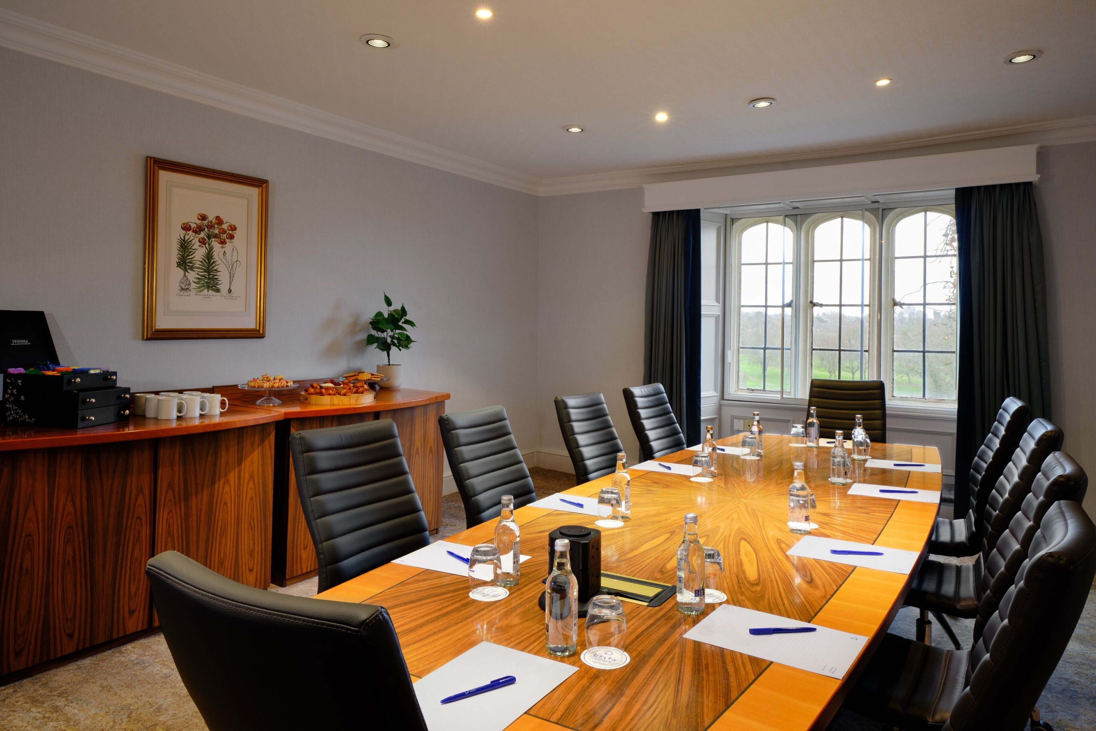 Une salle de conférence avec une longue table, des fauteuils en cuir noir et un bureau en bois sur lequel se trouvent un ordinateur et une plante.