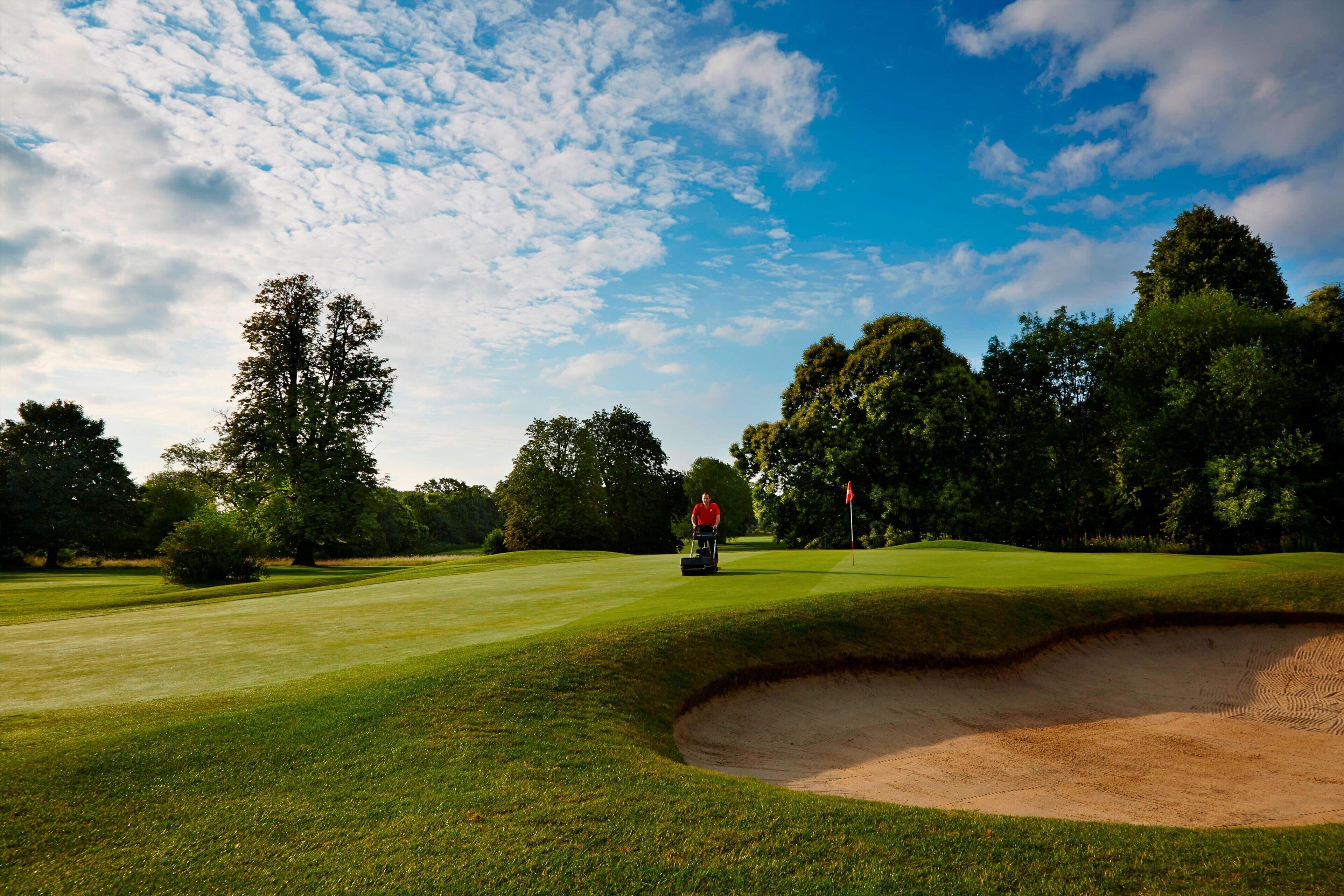 A golf course with a sand bunker, trees, and a clear sky.