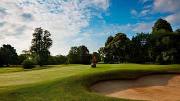 Un parcours de golf avec un bunker de sable, des arbres et un ciel dégagé.