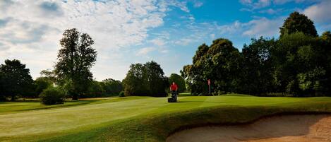 A golf course with a sand bunker, trees, and a clear sky.