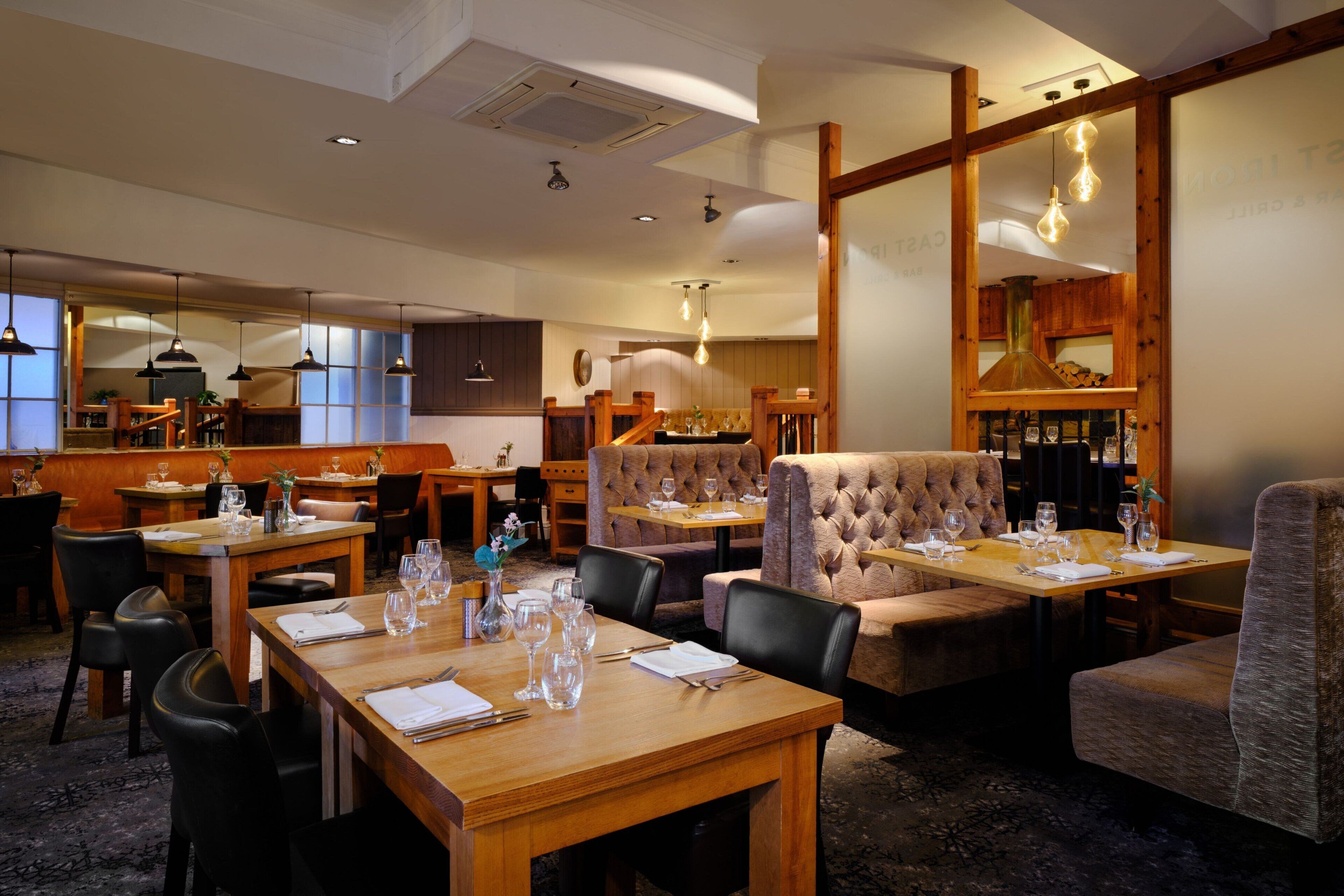 A restaurant with wooden tables and chairs, a bar area, and a seating section with cushioned booths.