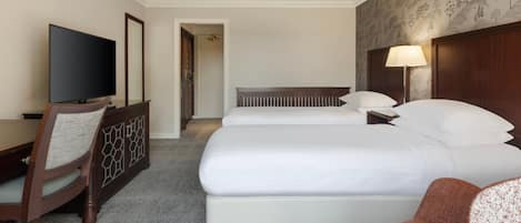 Ein Hotelzimmer mit zwei Betten, einem Schreibtisch mit Fernseher, einem Sessel und einer Lampe.