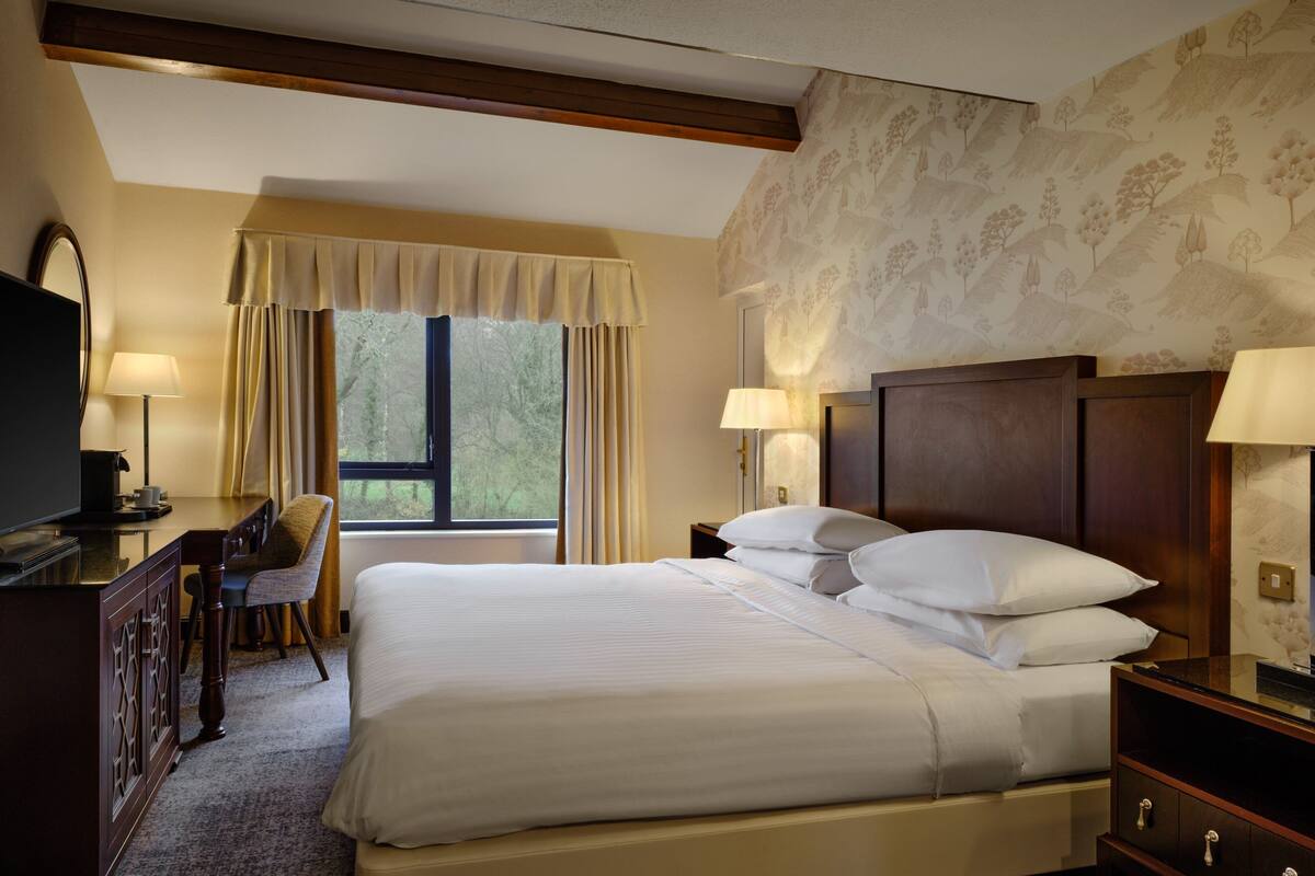 A hotel room with a large bed, a desk with a chair, a television, and a window with curtains.