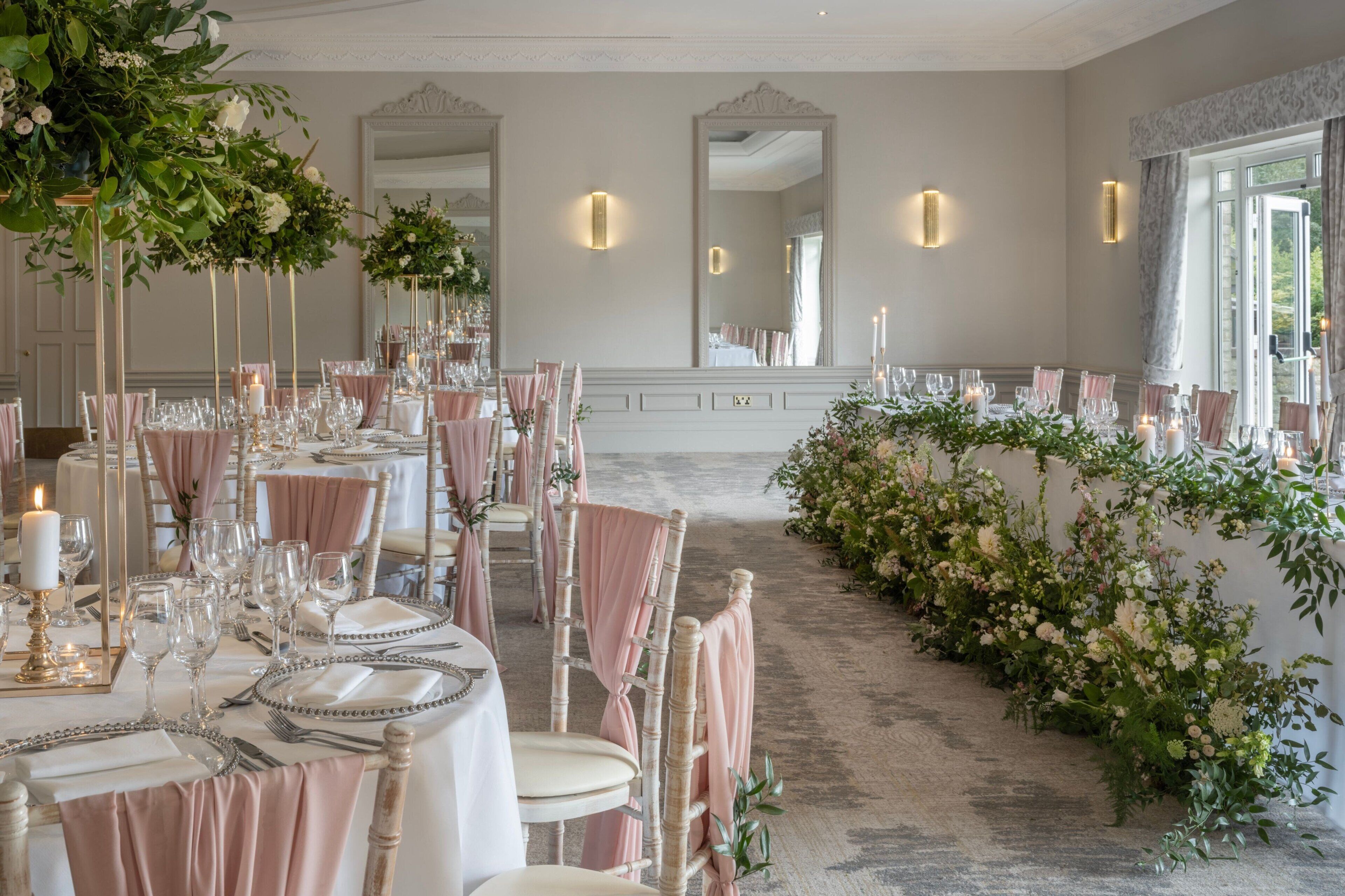 A formal dining room with long tables, elegant chairs, and floral decorations.