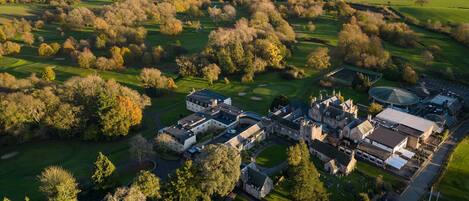 An aerial view of a golf course with a clubhouse, a parking area, and a large body of water in the background.