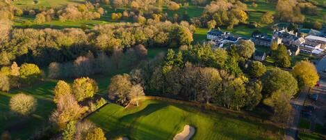 Oversigtsbillede af en golfbane med sandbunker, en bro i baggrunden og et boligområde med huse.