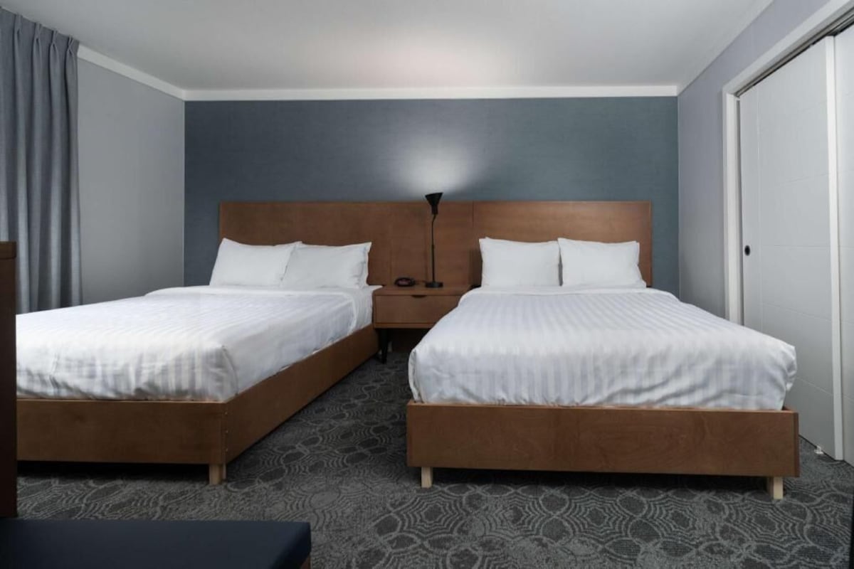 A hotel room with two single beds, a nightstand, a lamp, and a door.