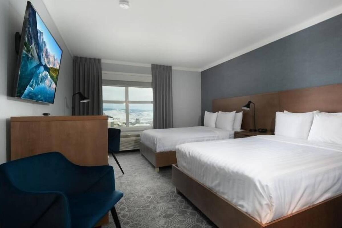 A hotel room with two beds, a desk, a chair, a TV, and a large window.
