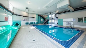 An indoor swimming pool with a slide, tiled flooring, and a staircase leading to an upper level.