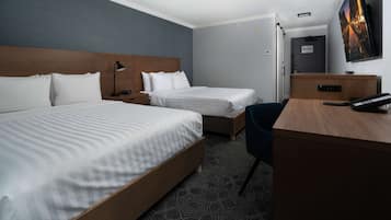 A hotel room with two single beds, a desk, a chair, a TV, and a door leading to a bathroom.