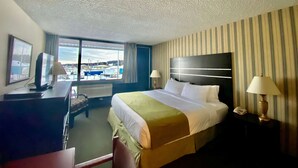 A hotel room with a large bed, a desk with a computer, a telephone, and a window with a view of the outside.