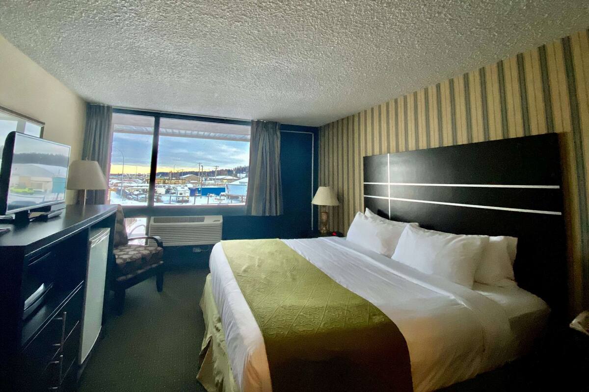 Ein Hotelzimmer mit einem großen Bett, einem Schreibtisch mit Fernseher, einem Sessel und Blick auf einen Hafen durch ein großes Fenster.