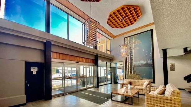 A spacious lobby with a high ceiling, large windows, and a view of the outdoors. There are two seating areas with checkered sofas and a coffee table.