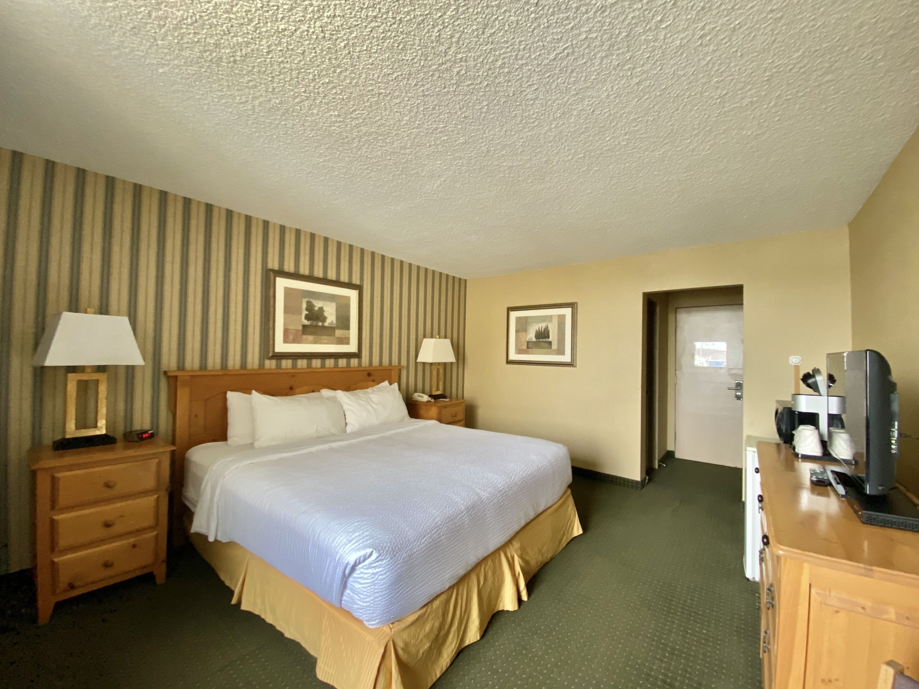 A hotel room with a large bed, two bedside tables with lamps, a television, and a coffee machine.