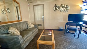 A living room with a sofa, a glass coffee table, a television, and a wall-mounted decoration. - Ramada by Wyndham Whitecourt (Whitecourt)
