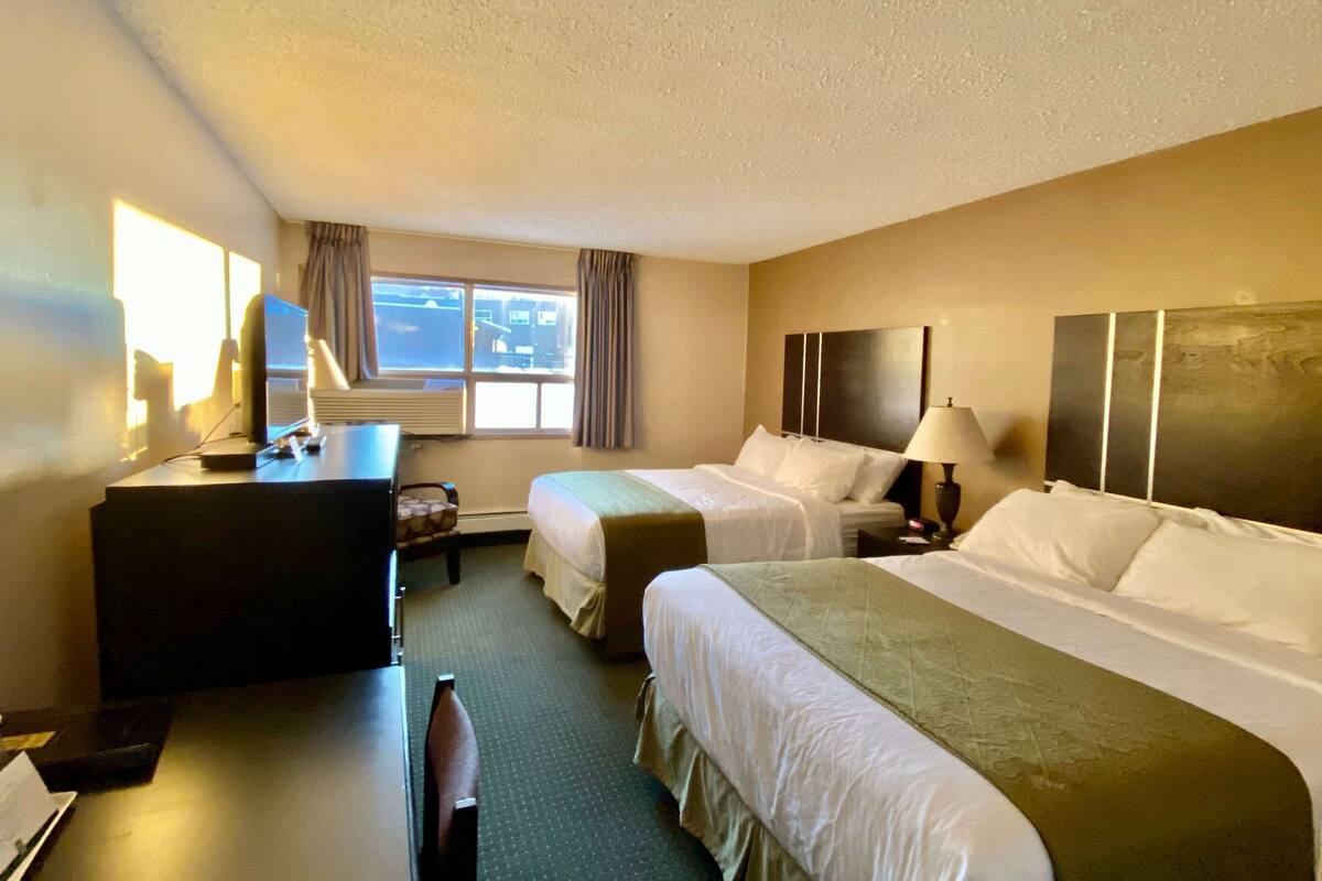 Ein Hotelzimmer mit zwei Betten, einem Schreibtisch, einem Stuhl, einer Lampe und einem Fenster mit Vorhängen.
