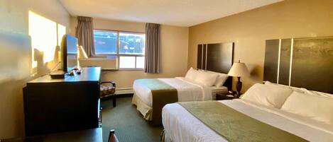 Quarto de hotel com duas camas, uma mesa, uma cadeira, um abajur e uma janela com cortinas.