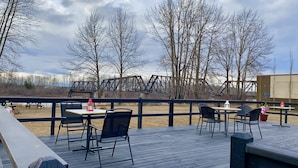 An outdoor deck with tables and chairs, overlooking a bridge and trees.