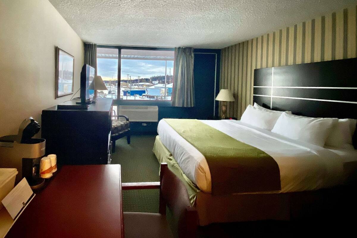 Ein Hotelzimmer mit Bett, Schreibtisch, Stuhl, Lampe und Blick nach draußen.