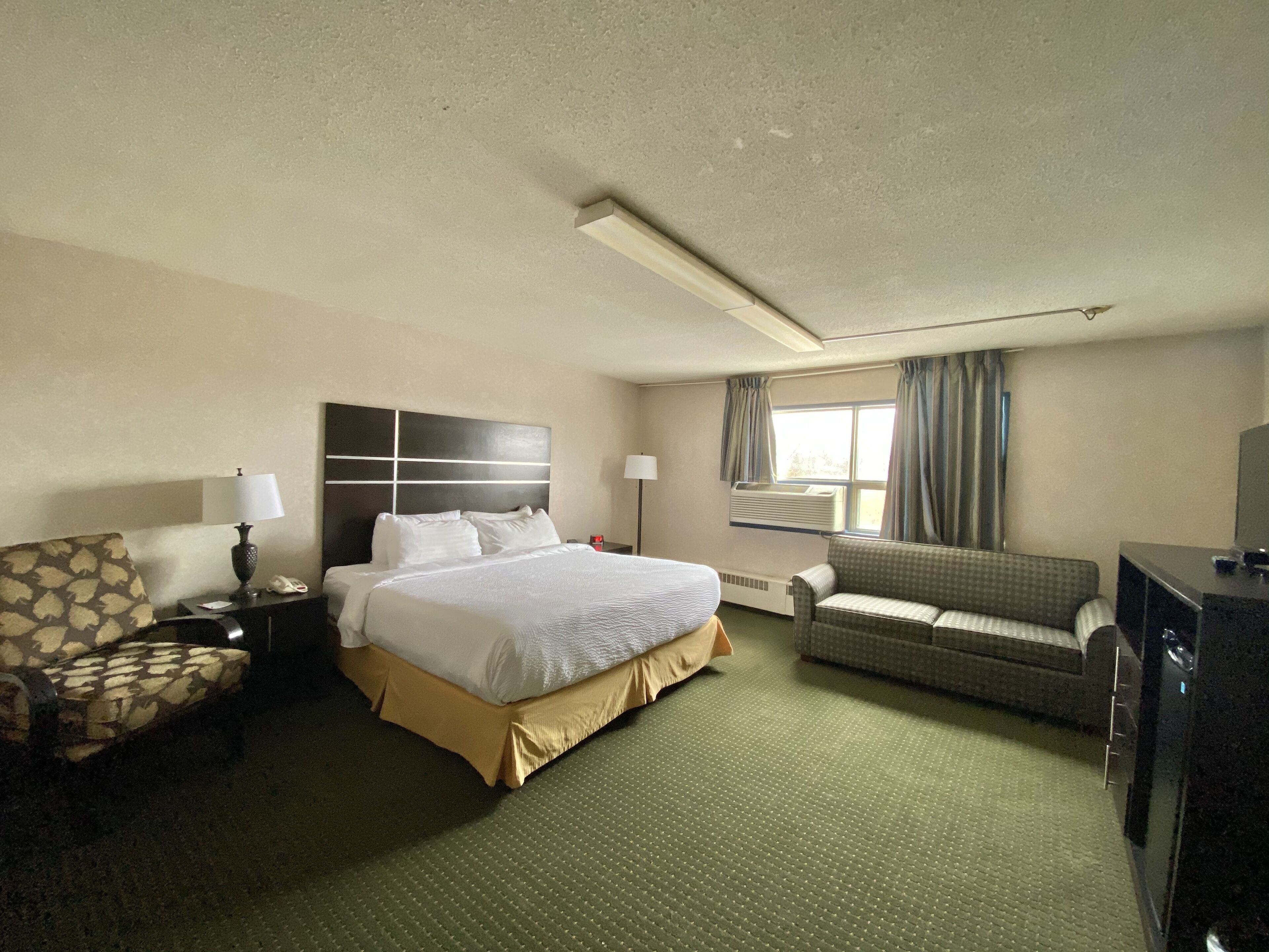 A hotel room with a large bed, a sofa, a desk, and a television.