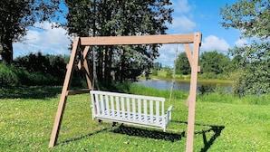 A wooden swing set with a white bench in a grassy area near a body of water. - Ramada by Wyndham Whitecourt (Whitecourt)