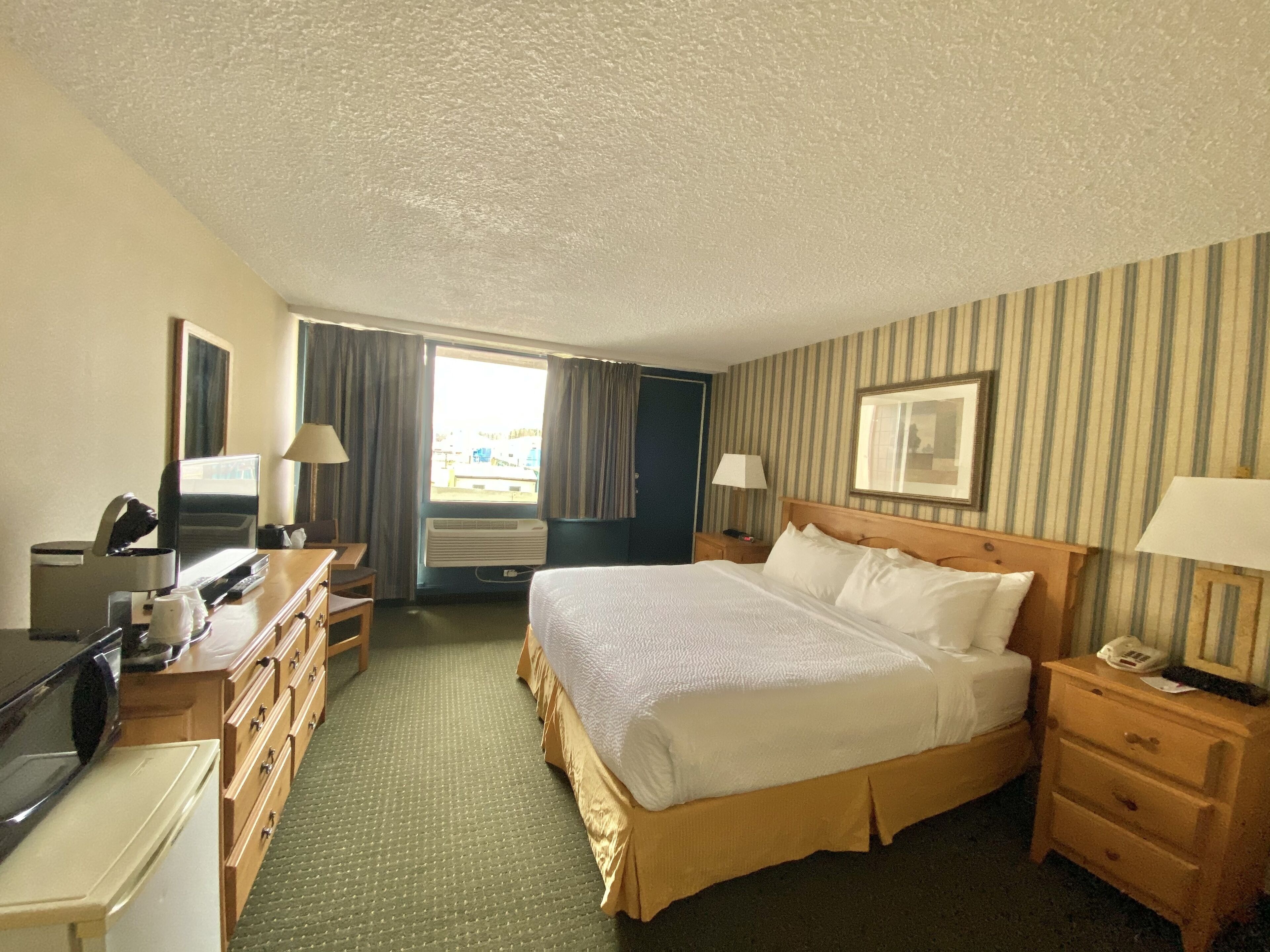 A hotel room with a bed, a desk, a chair, a dresser, a TV, and a window with curtains.