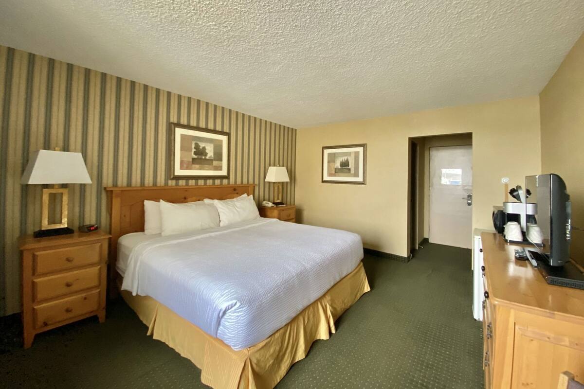 Ein Hotelzimmer mit einem großen Bett, zwei Nachttischen mit Lampen, einem Schminktisch, einem Fernseher und gerahmten Bildern an der Wand.