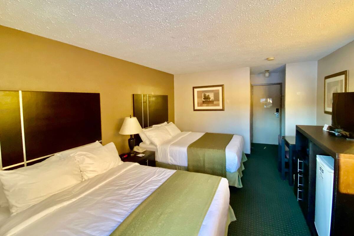 Ein Hotelzimmer mit zwei Betten, einem Schreibtisch, einem Stuhl, einer Lampe und einem Kühlschrank.