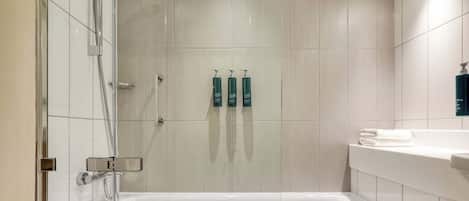 A modern bathroom with a glass-enclosed shower, a white bathtub, and a vanity with a mirror and towel rack.