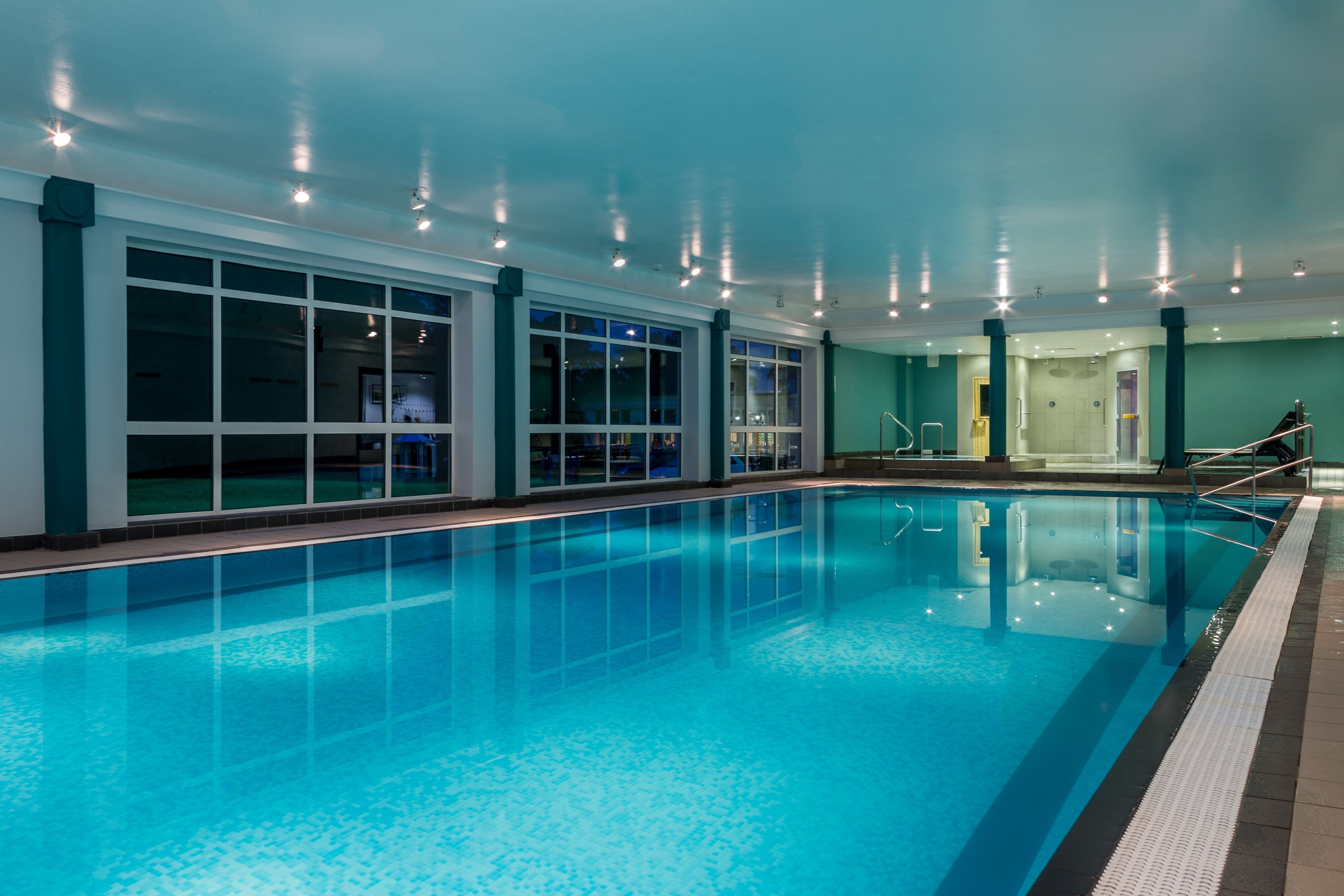 An indoor swimming pool with clear water, surrounded by large windows and a teal-colored wall.
