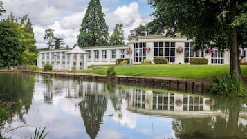 A large, white building with multiple windows and a pond in front.