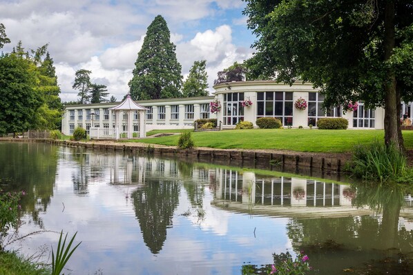 A large, white building with multiple windows and a pond in front. - DoubleTree by Hilton Cheltenham-Cotswolds (Cheltenham)