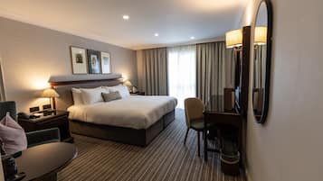 A hotel room with a large bed, bedside tables with lamps, a desk with a chair, and a large mirror.