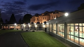 Un hôtel doté d’une grande façade en verre, d’un espace extérieur aménagé pour s’asseoir et d’une pelouse bien éclairée.
