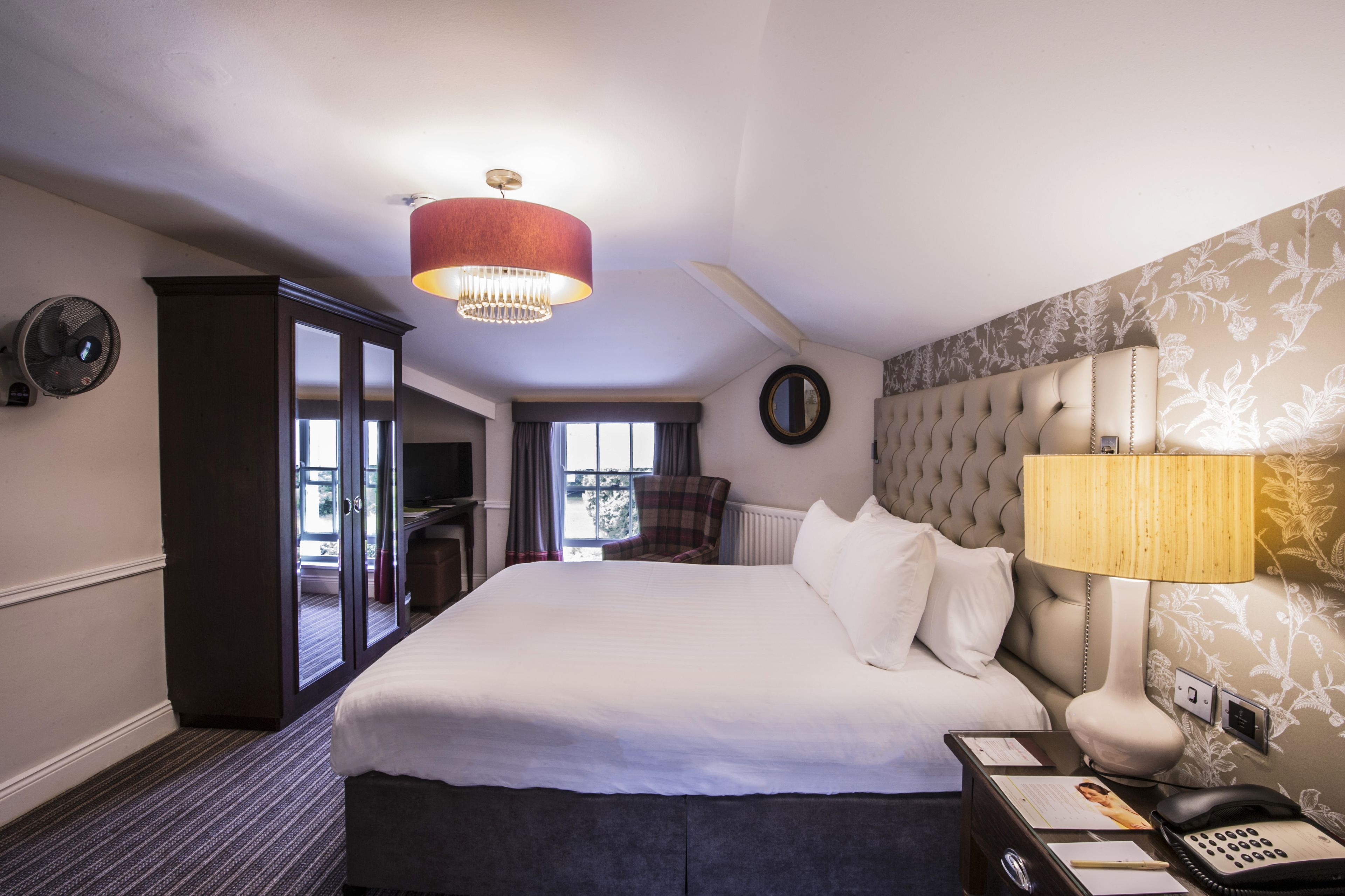 A hotel room with a large bed, a nightstand with a lamp, a wardrobe, and a view of the outdoors.