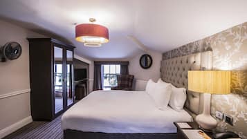 A hotel room with a large bed, a nightstand with a lamp, a wardrobe, and a view of the outdoors.