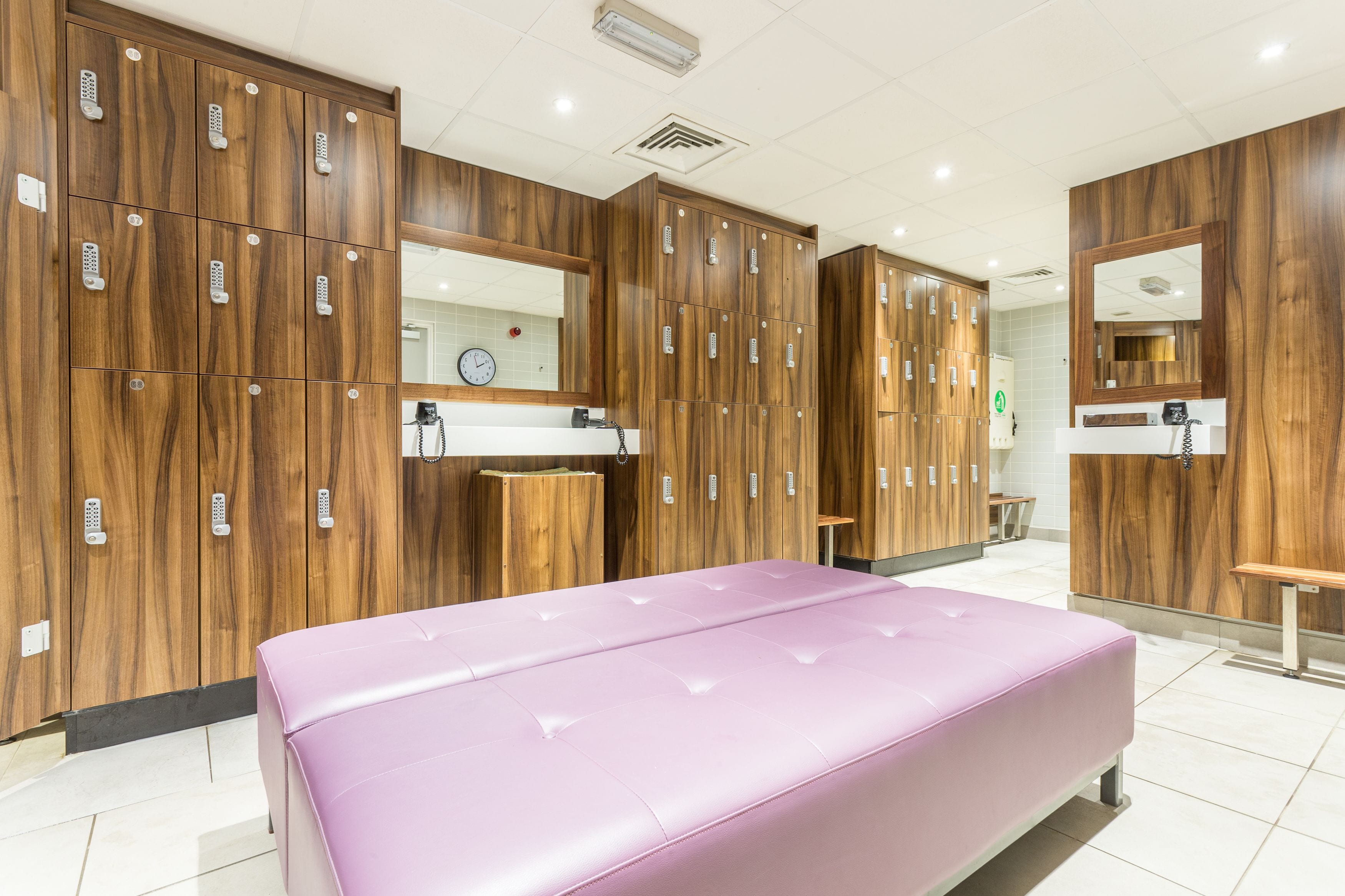 A modern bathroom with wooden lockers, a bench, and a vanity area.
