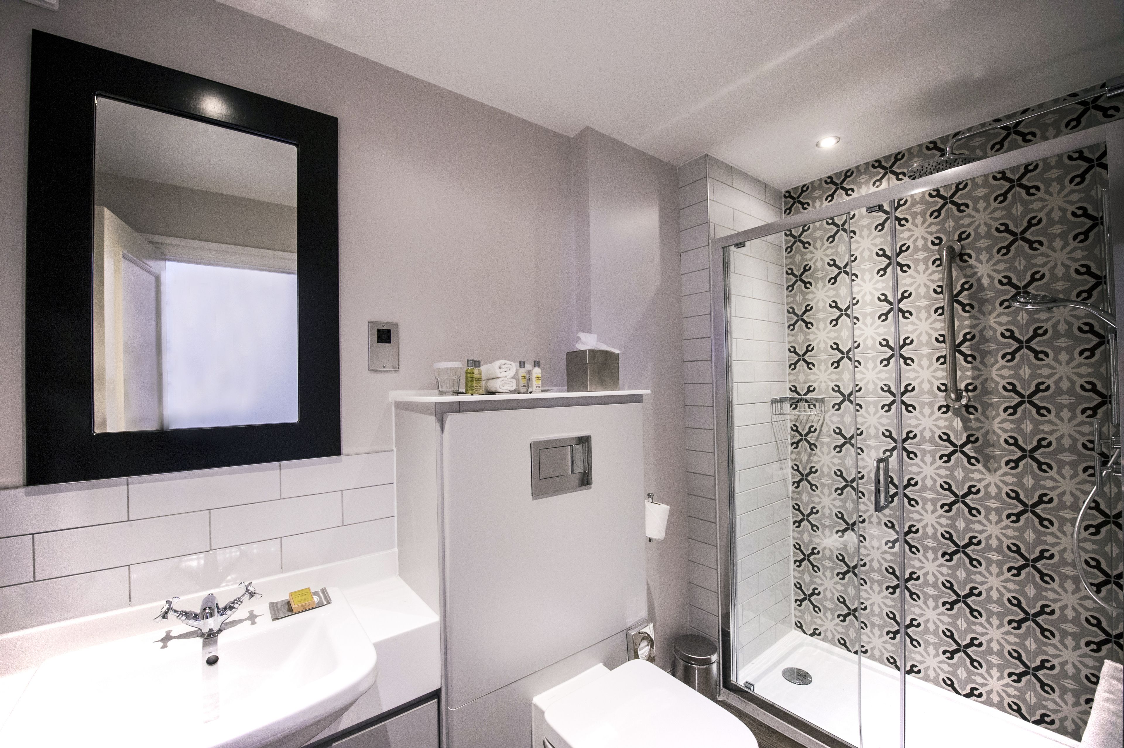 A modern bathroom with two sinks, a large mirror, and a shower with patterned tiles.