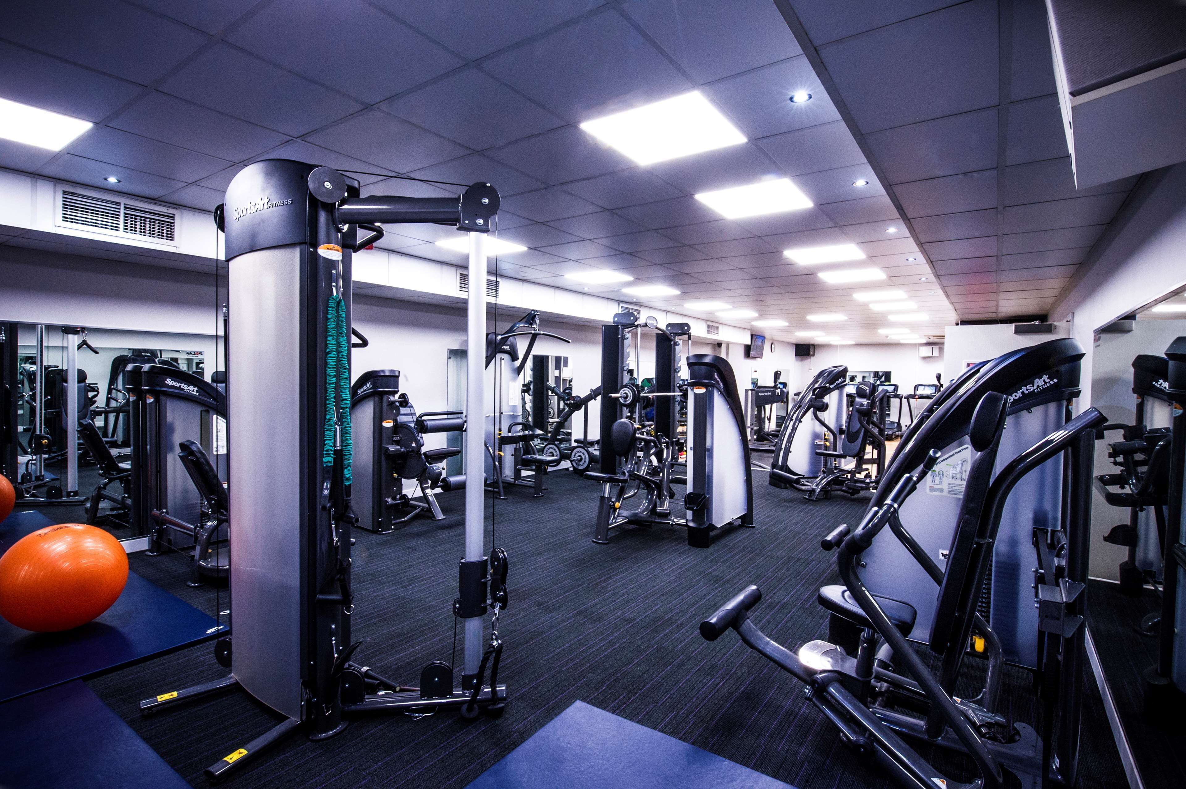 Ein Fitnessstudio mit verschiedenen Trainingsgeräten, Spiegeln und einer blauen Matte.