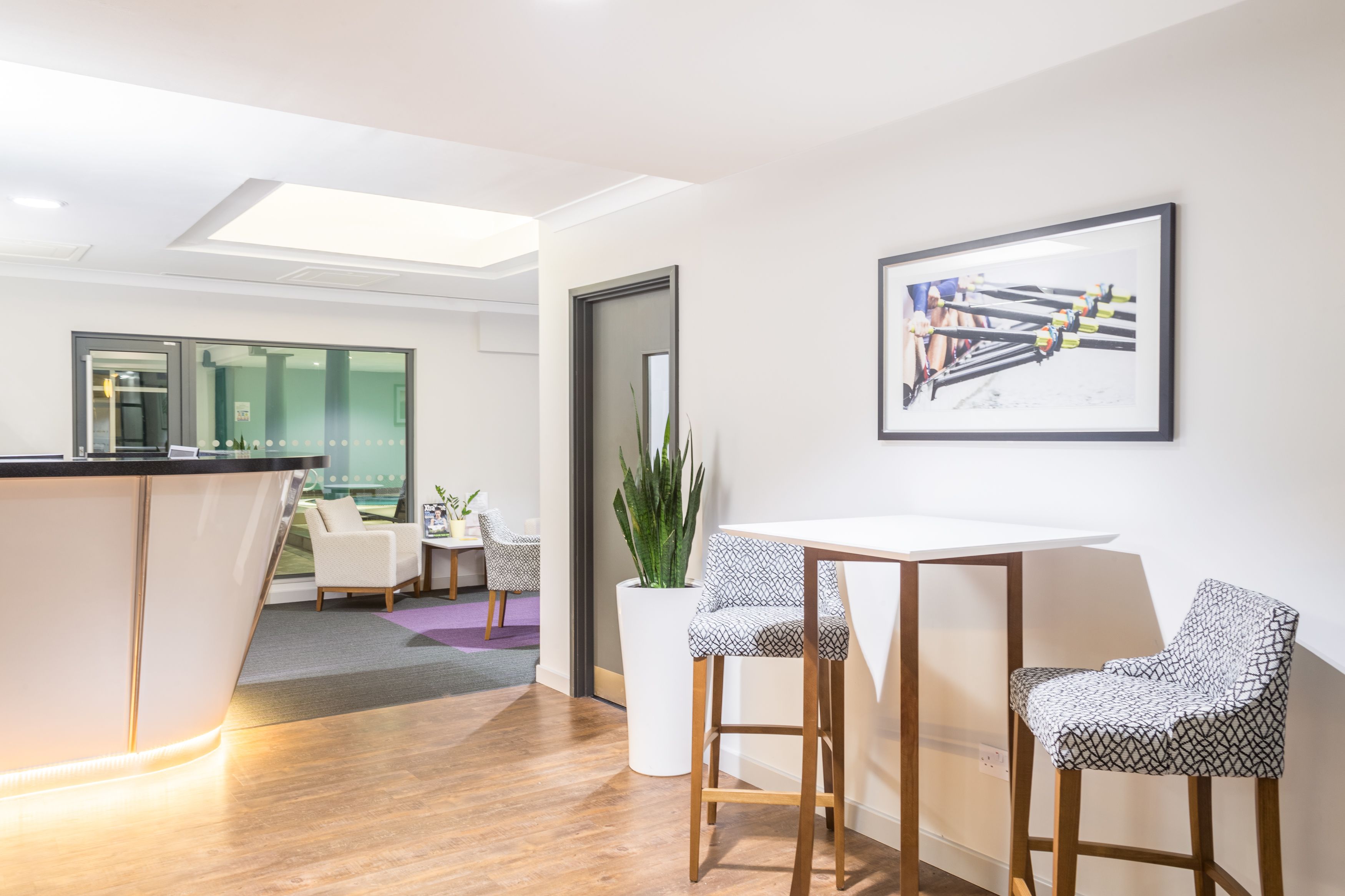 A modern office space with a reception desk, two bar stools, a white table, and a framed picture on the wall.