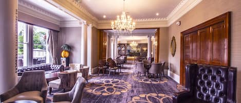 A spacious lobby with a chandelier, leather seating, and a patterned carpet.