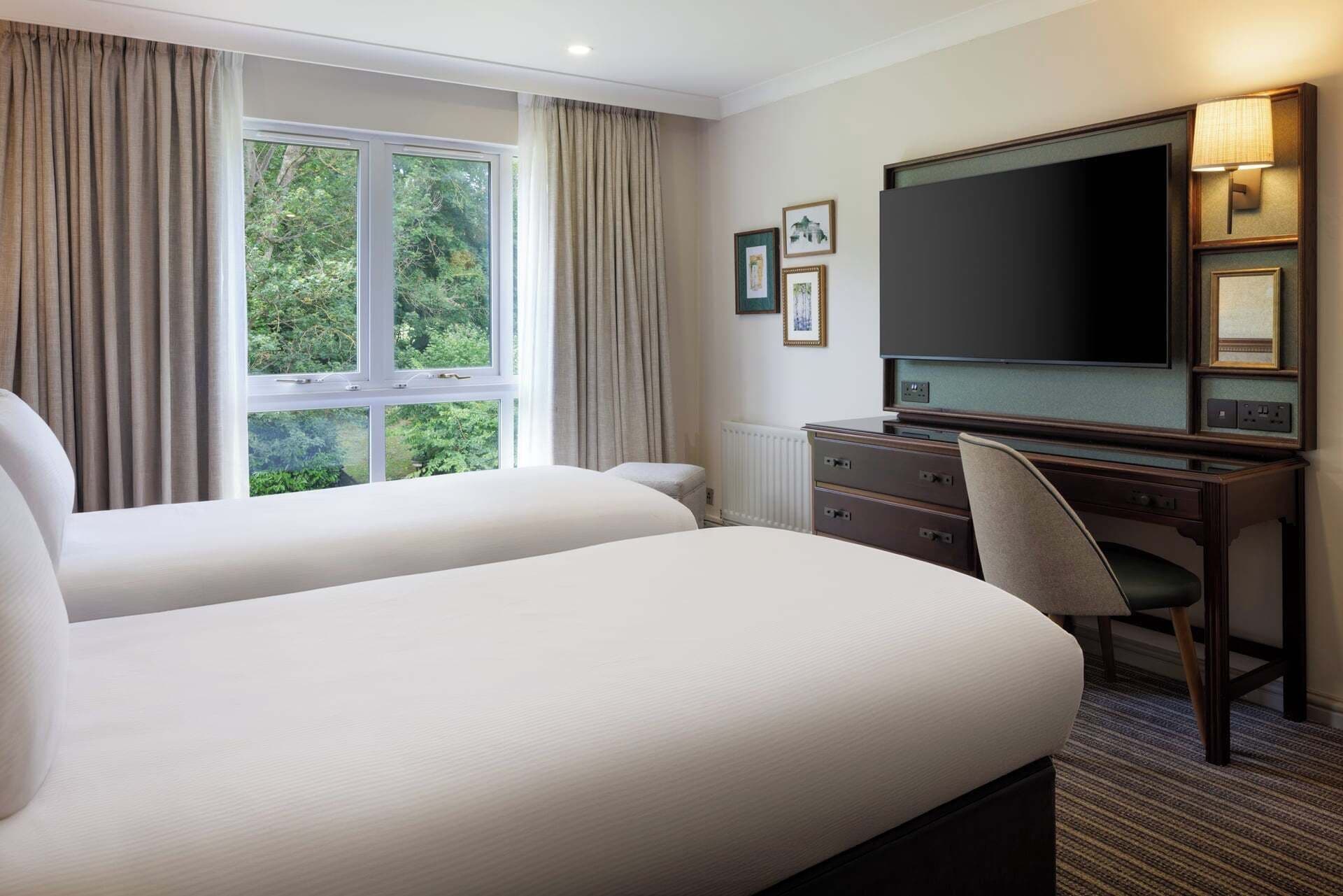 Een hotelkamer met twee bedden, een bureau met een televisie en een raam met gordijnen.