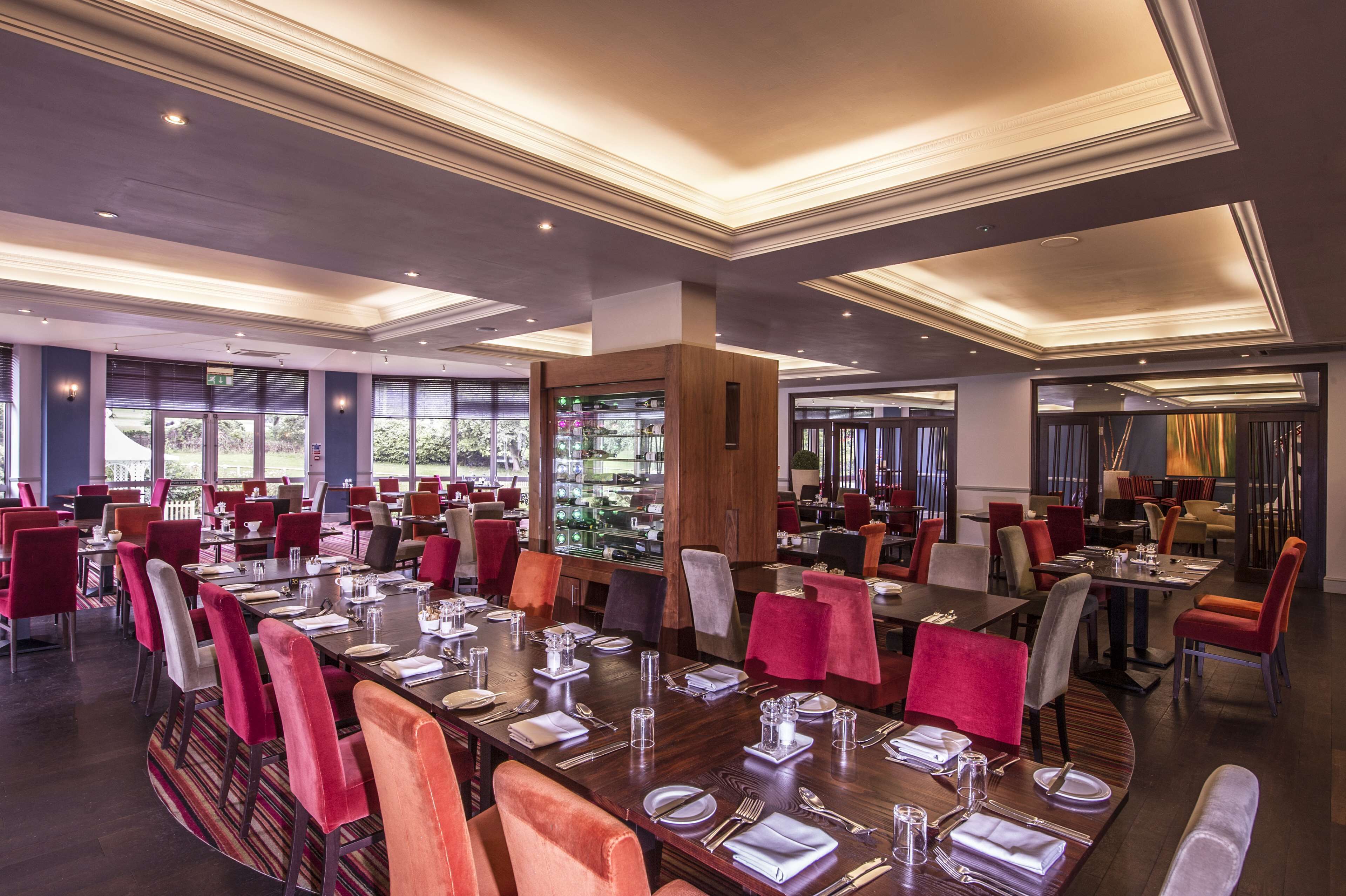 A spacious dining area with multiple tables set for dining, large windows, and a modern ceiling design.