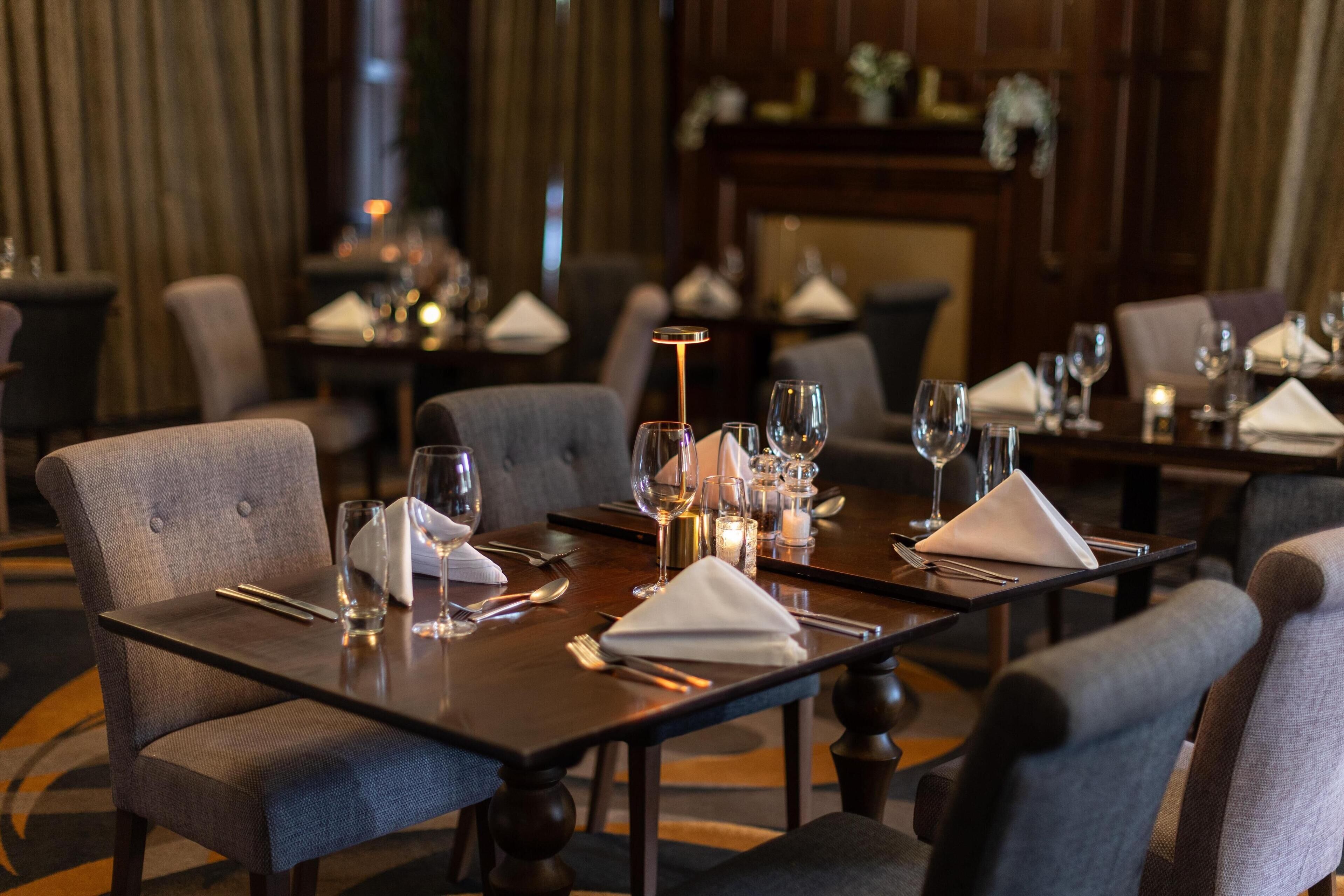 A dining area with tables set for two, each with a white napkin, cutlery, and wine glasses.