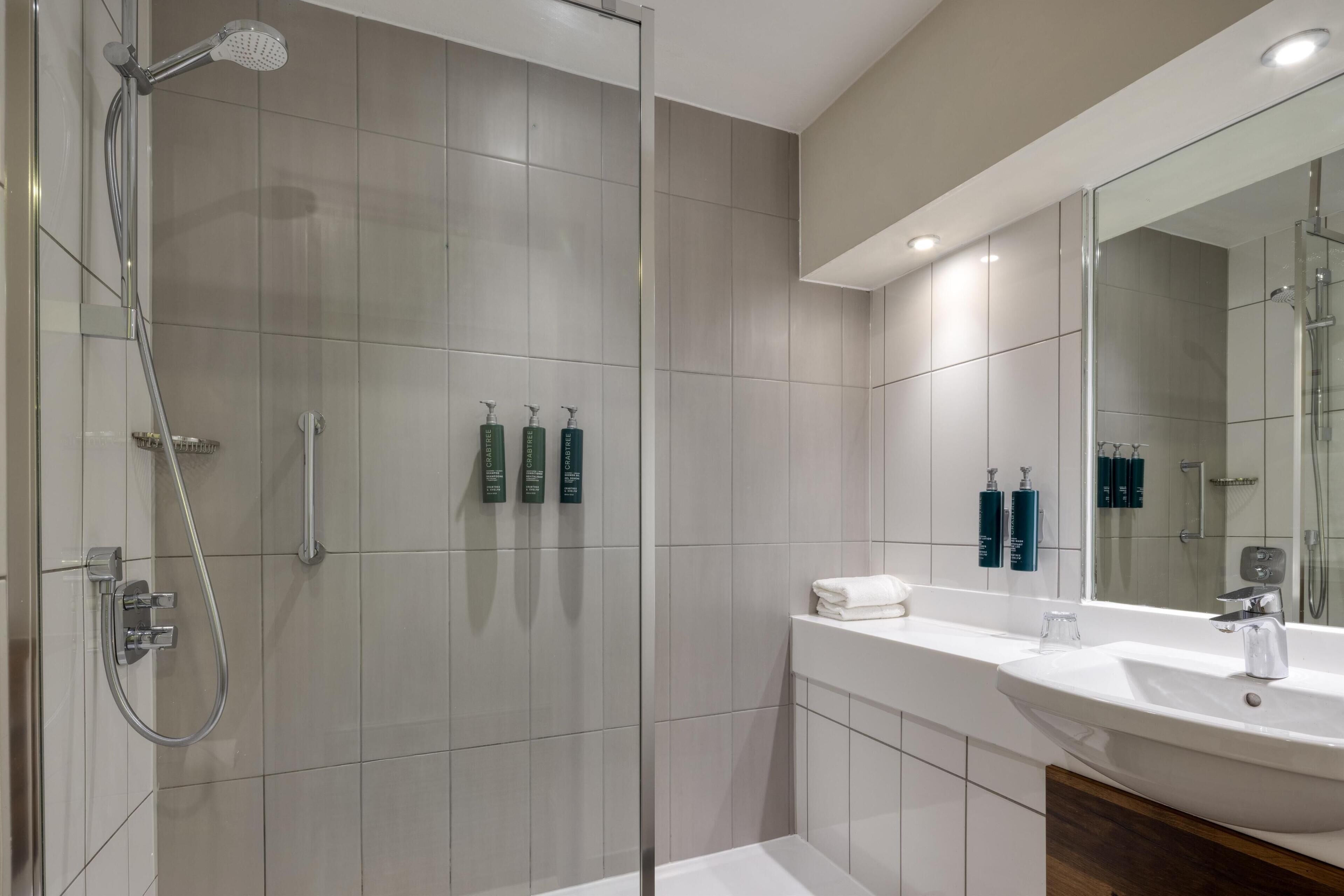 Une salle de bain moderne avec une douche à parois de verre, un lavabo blanc et un miroir au-dessus.
