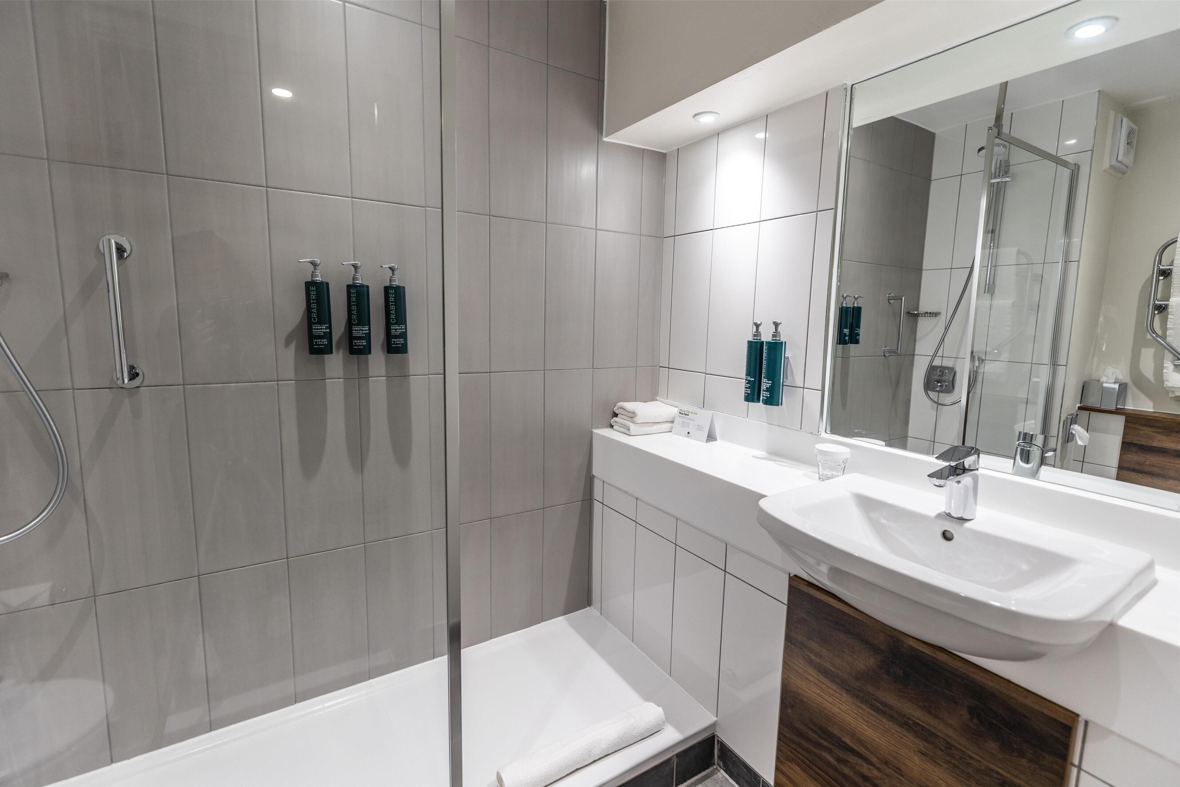 A modern bathroom with a glass-enclosed shower, a white sink, and a vanity with toiletries.