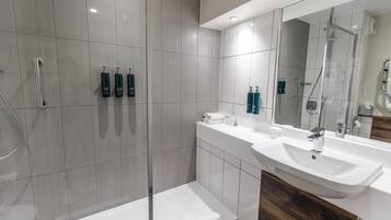 A modern bathroom with a glass-enclosed shower, a white sink, and a vanity with toiletries.