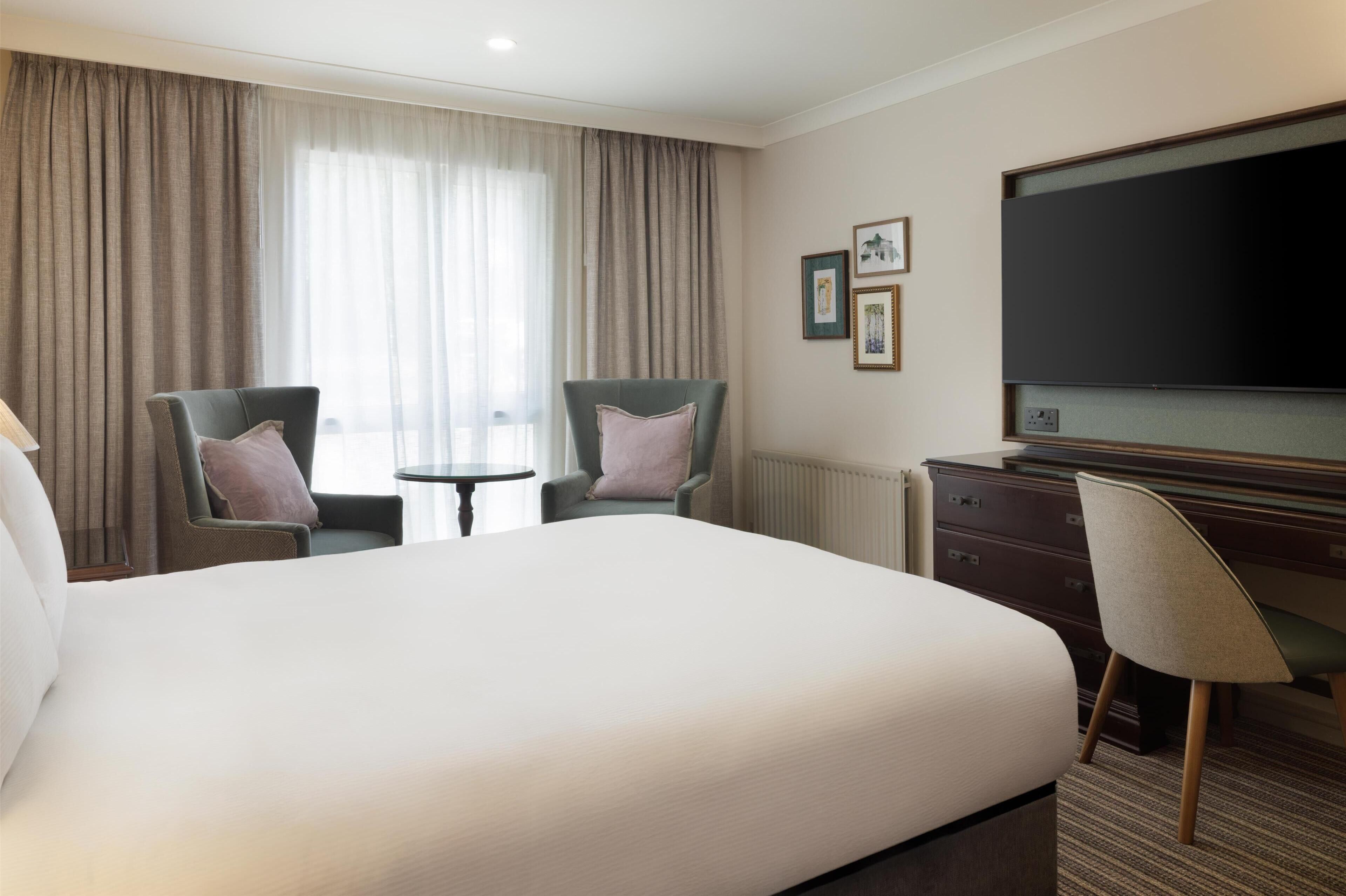 Habitación de hotel con una cama grande, dos sillones, una mesita, un televisor y un aparador.